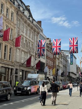 Street view with Union Jack flags, people walking, and classic architecture in London.