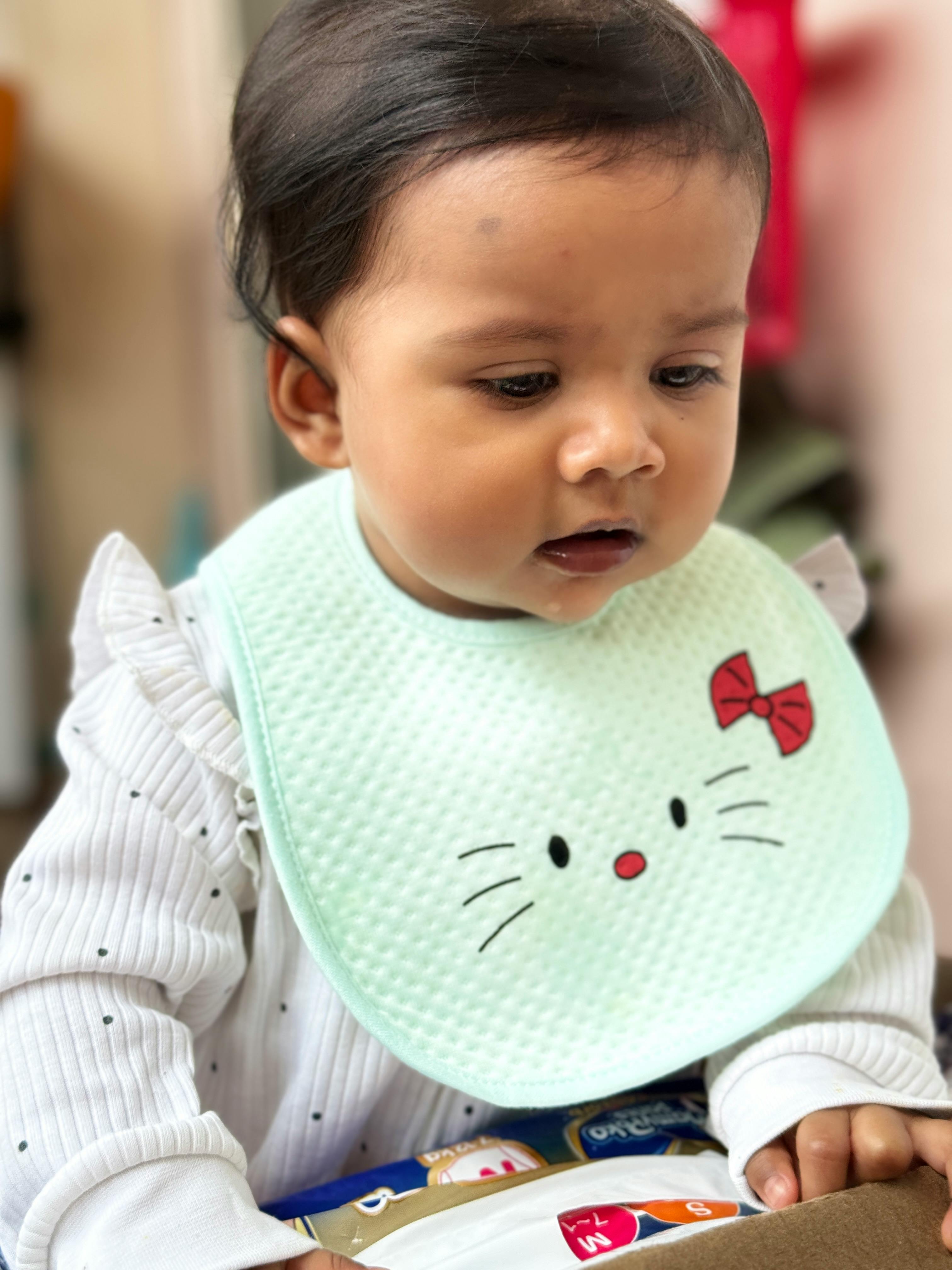 A charming baby wearing a cute bib indoors, capturing innocence and curiosity.
