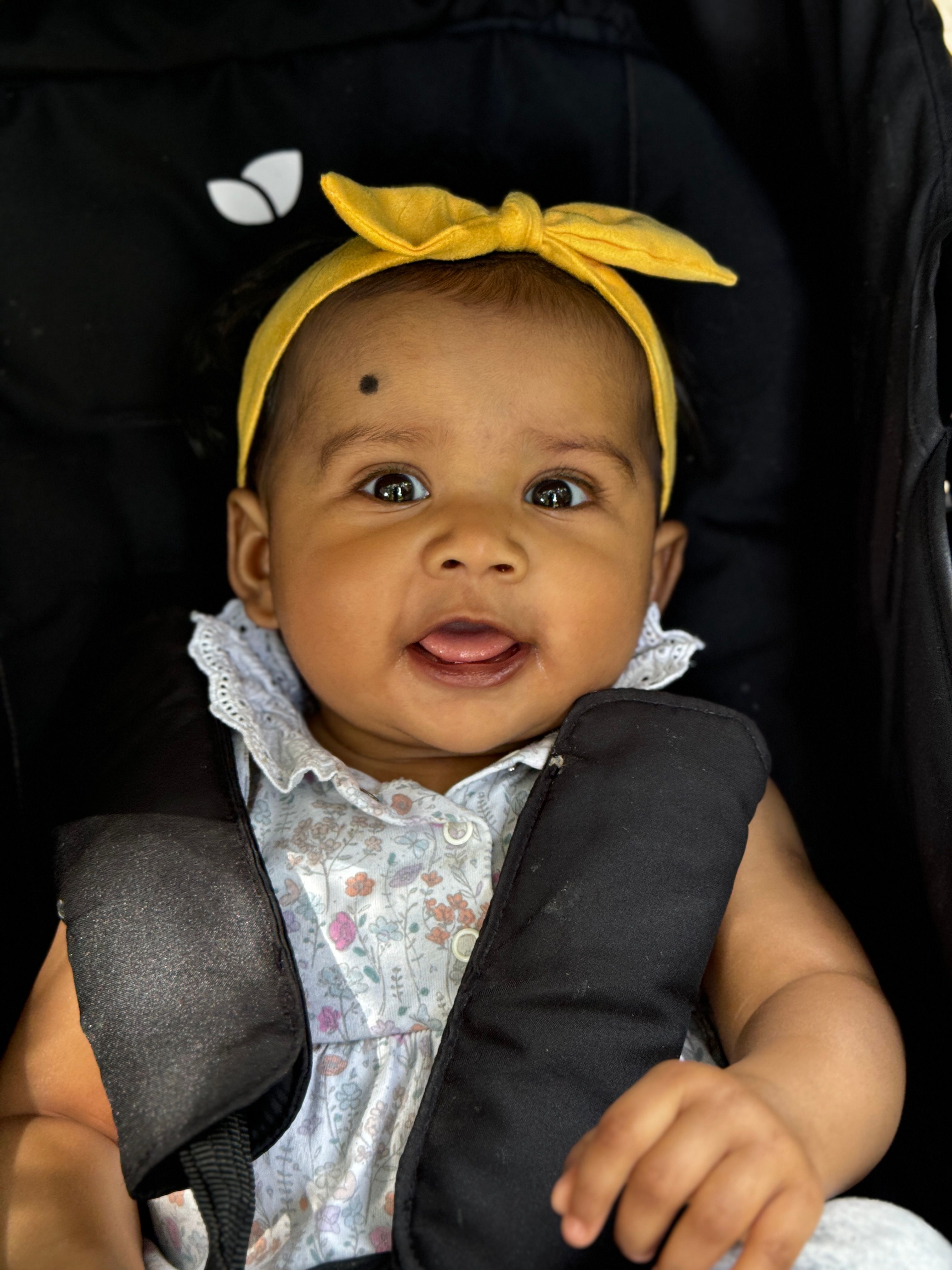 Adorable baby wearing a floral dress and yellow headband, sitting in a stroller.