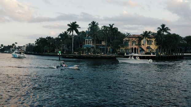Tranquil boating scene on a tropical waterfront with luxurious homes.