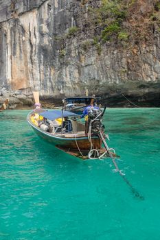 A traditional longtail boat on turquoise waters near a rugged limestone cliff on a sunny day.