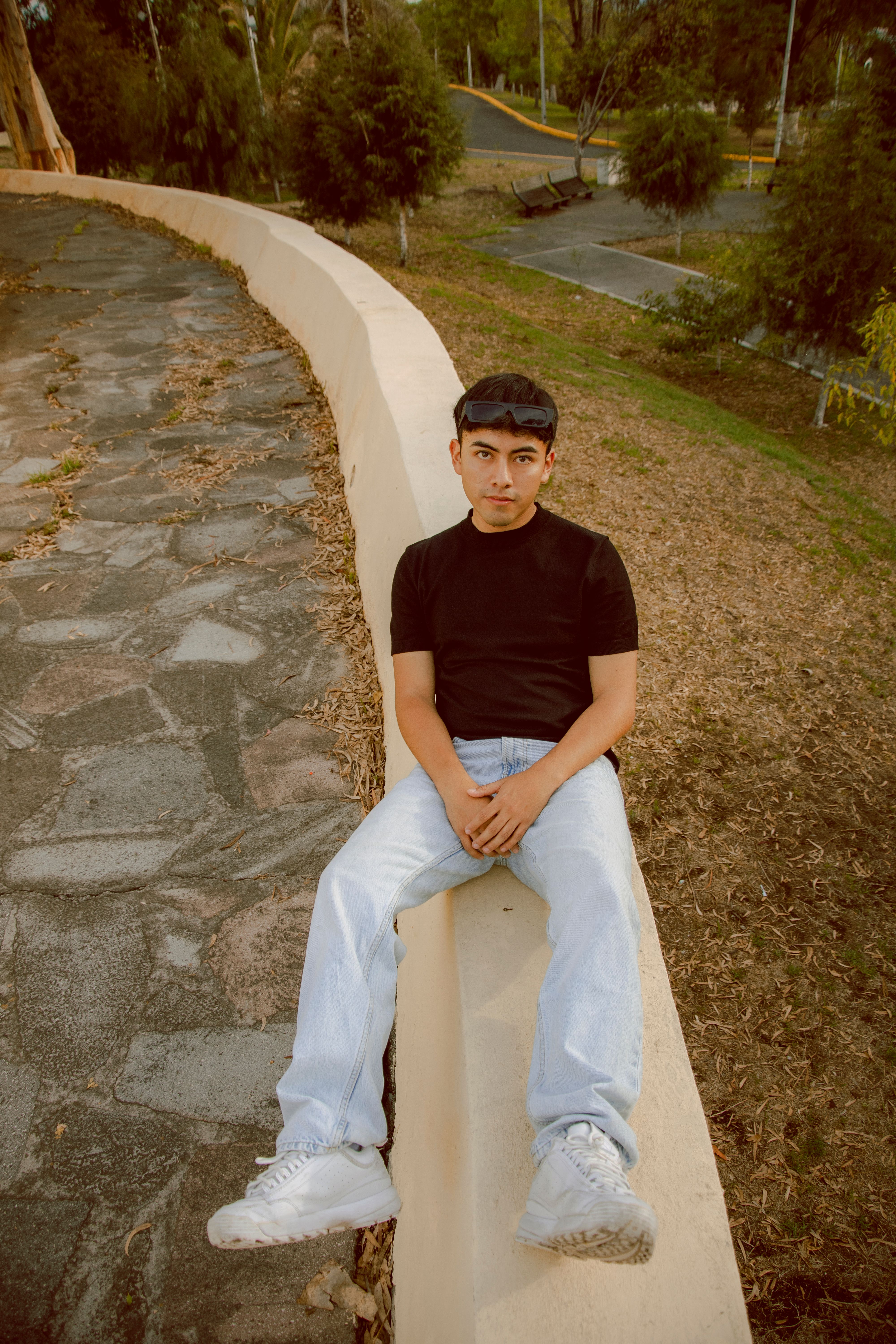 Young male sitting casually on a stone wall in an outdoor park setting.