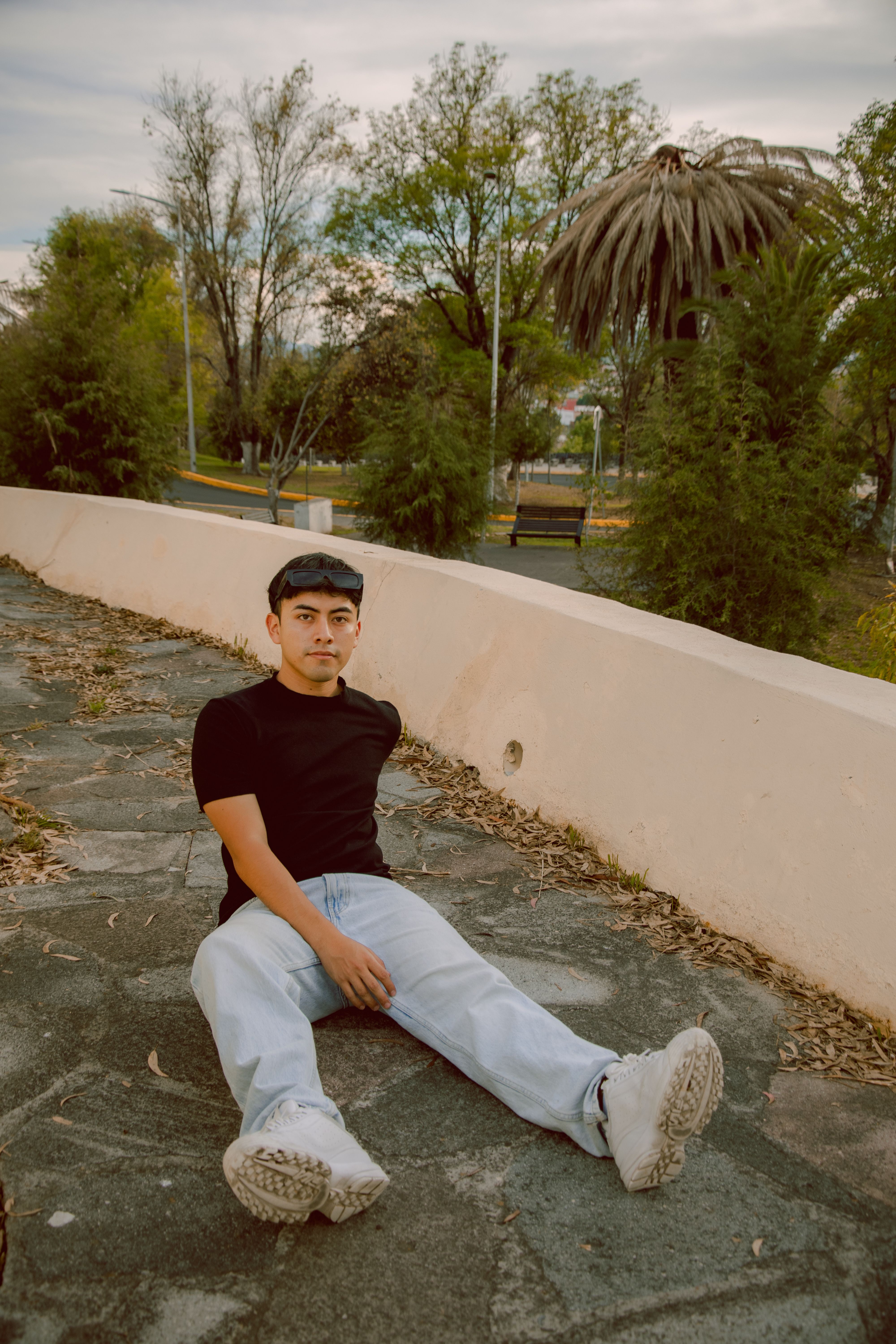 Man sitting casually on stone pavement in a serene urban park at day, exuding a relaxed mood.
