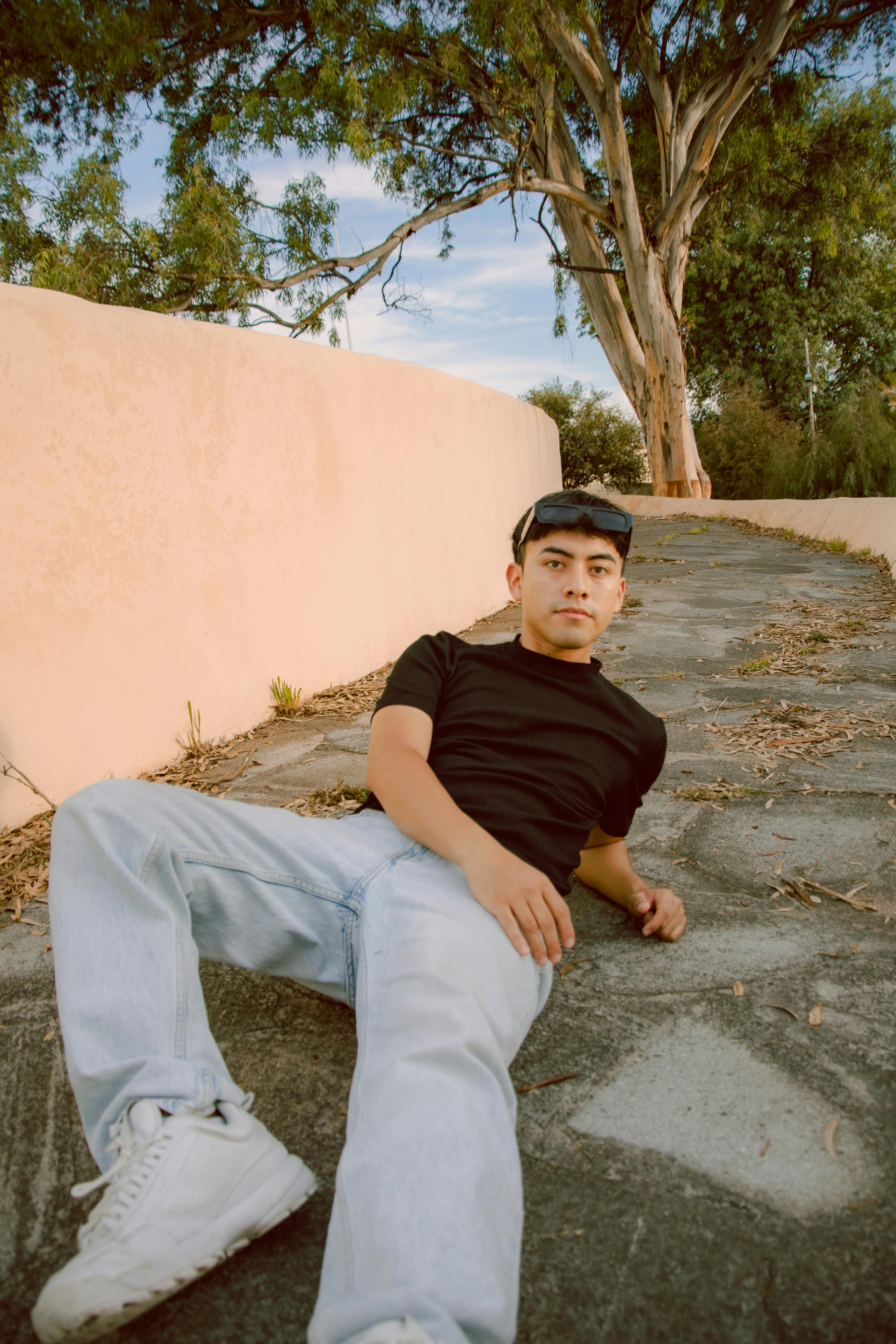 A young man in casual attire relaxes on a stone path outdoors in a serene environment.