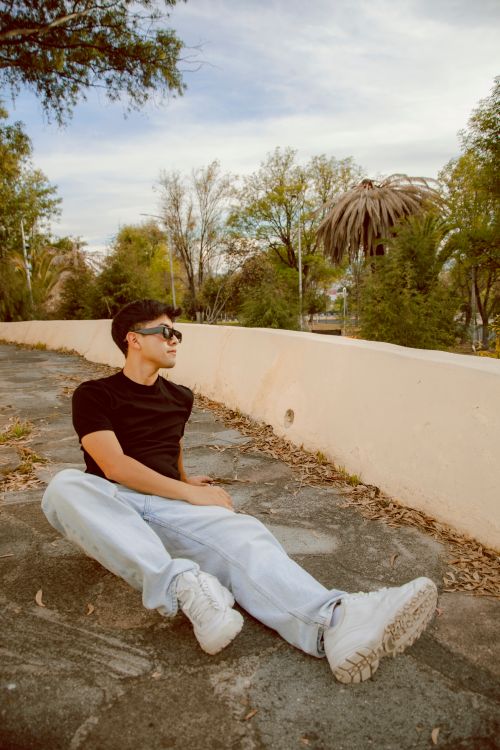 Free Young man in casual attire sitting outdoors on a sunny day, enjoying a moment of relaxation. Stock Photo