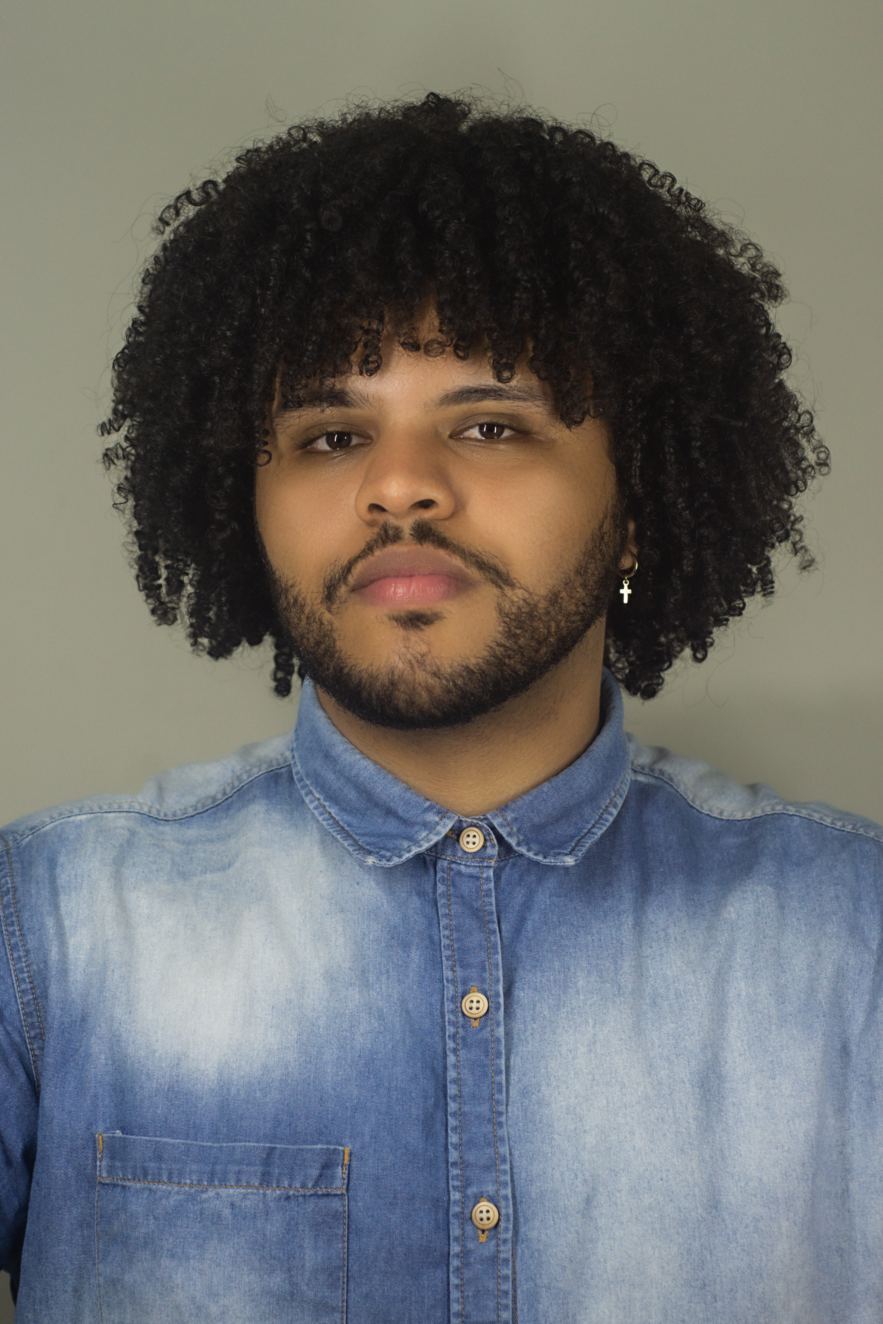 A close-up portrait of a man with curly hair wearing a denim shirt, exuding confidence.