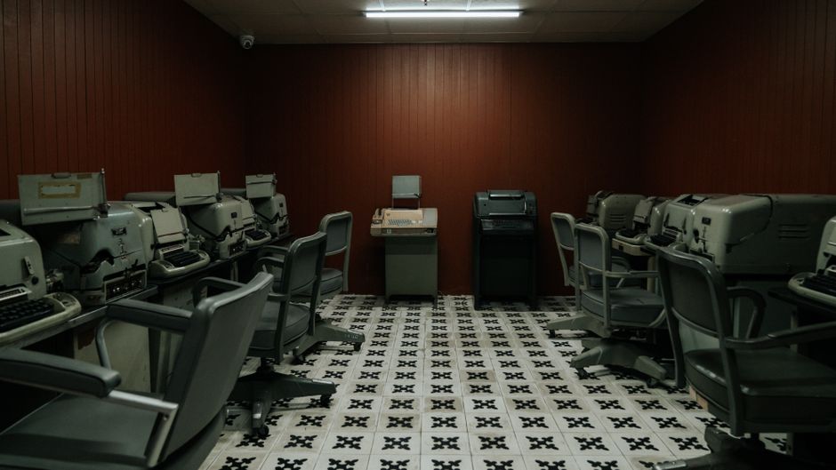 A vintage office room filled with old typewriters and chairs, evoking a 1940s-1960s era ambiance.