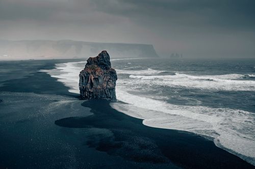 Free Moody scene of Iceland's black sand beach with striking sea stack and stormy skies. Stock Photo