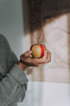 A close-up image of an apple being held by a hand indoors, showcasing its freshness.