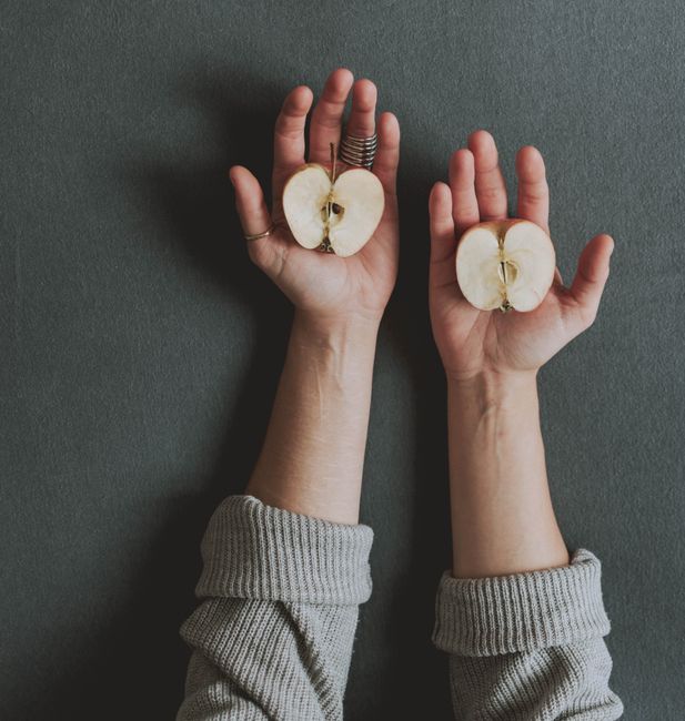 Two hands with rings showing off apple halves on a dark surface.