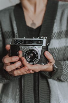 Close-up of a vintage analog camera held by a person wearing a cozy sweater, capturing retro nostalgia.