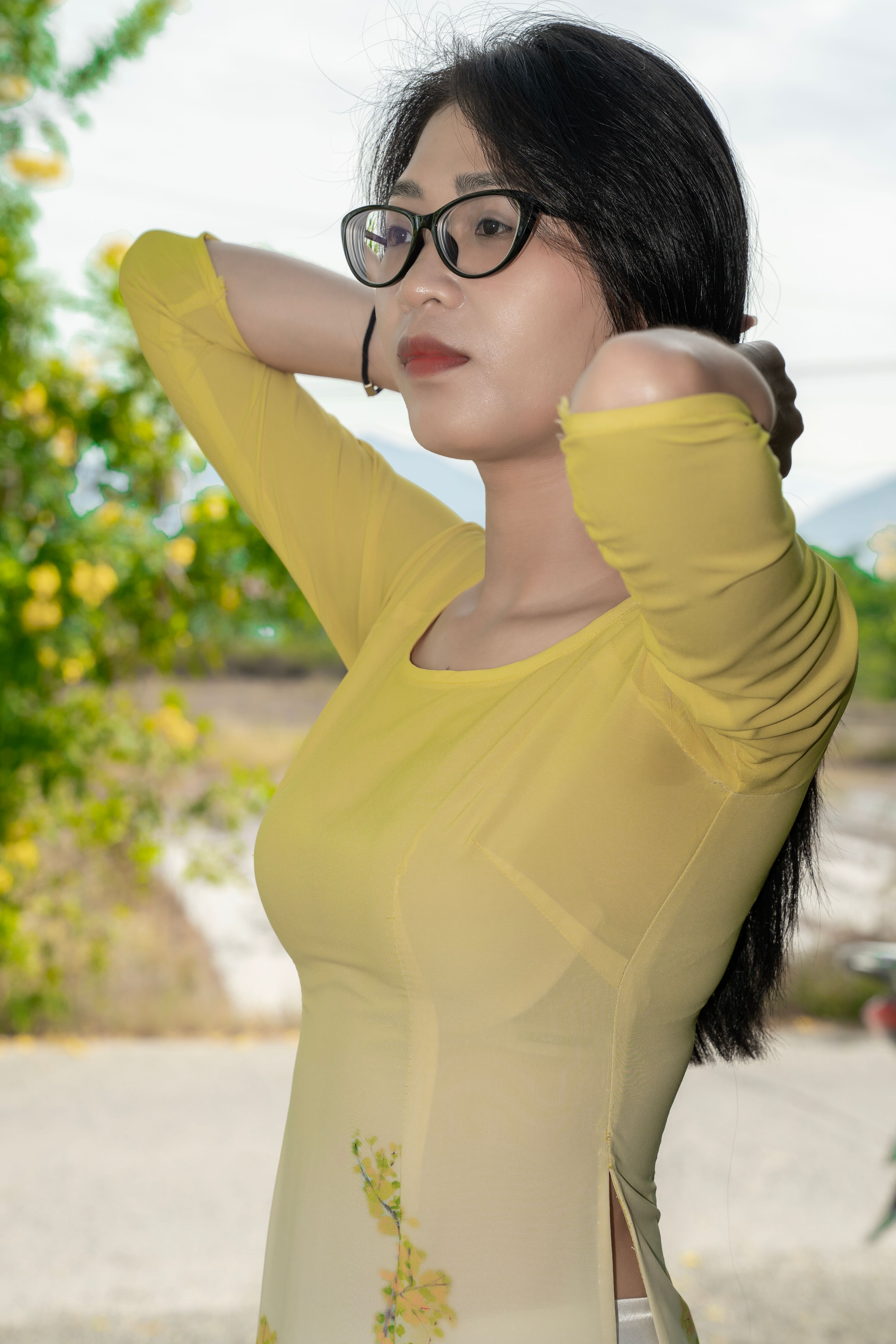 Stylish woman wearing yellow Ao Dai adjusts hair outdoors. Bright and vibrant.