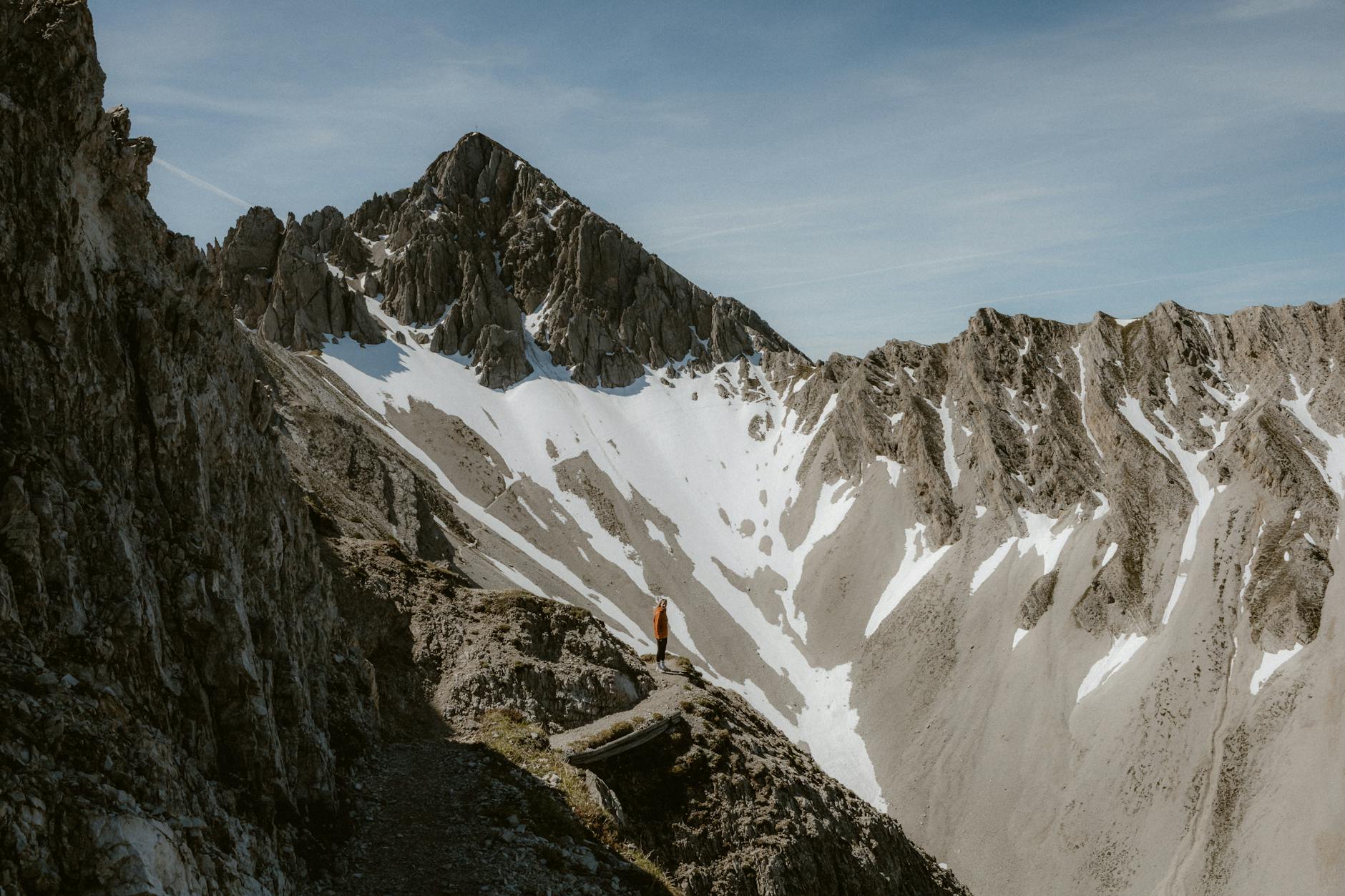 Adventure On A Budget: How To Travel With $500 1 a lone hiker stands amidst a dramatic mountain landscape under a clear sky.