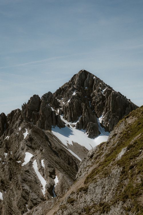 Free Rocky mountain peak with snow patches under a clear blue sky. Stock Photo