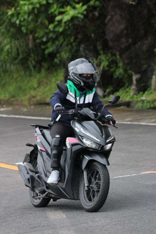 Free Man rides a scooter on a winding road surrounded by greenery. Stock Photo
