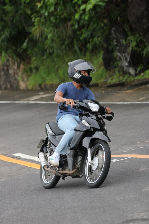 Free A man rides a motorcycle on a winding road, wearing a helmet for safety. Stock Photo