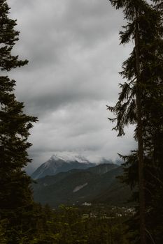 A tranquil mountain view with dark clouds, surrounded by lush trees and distant peaks.