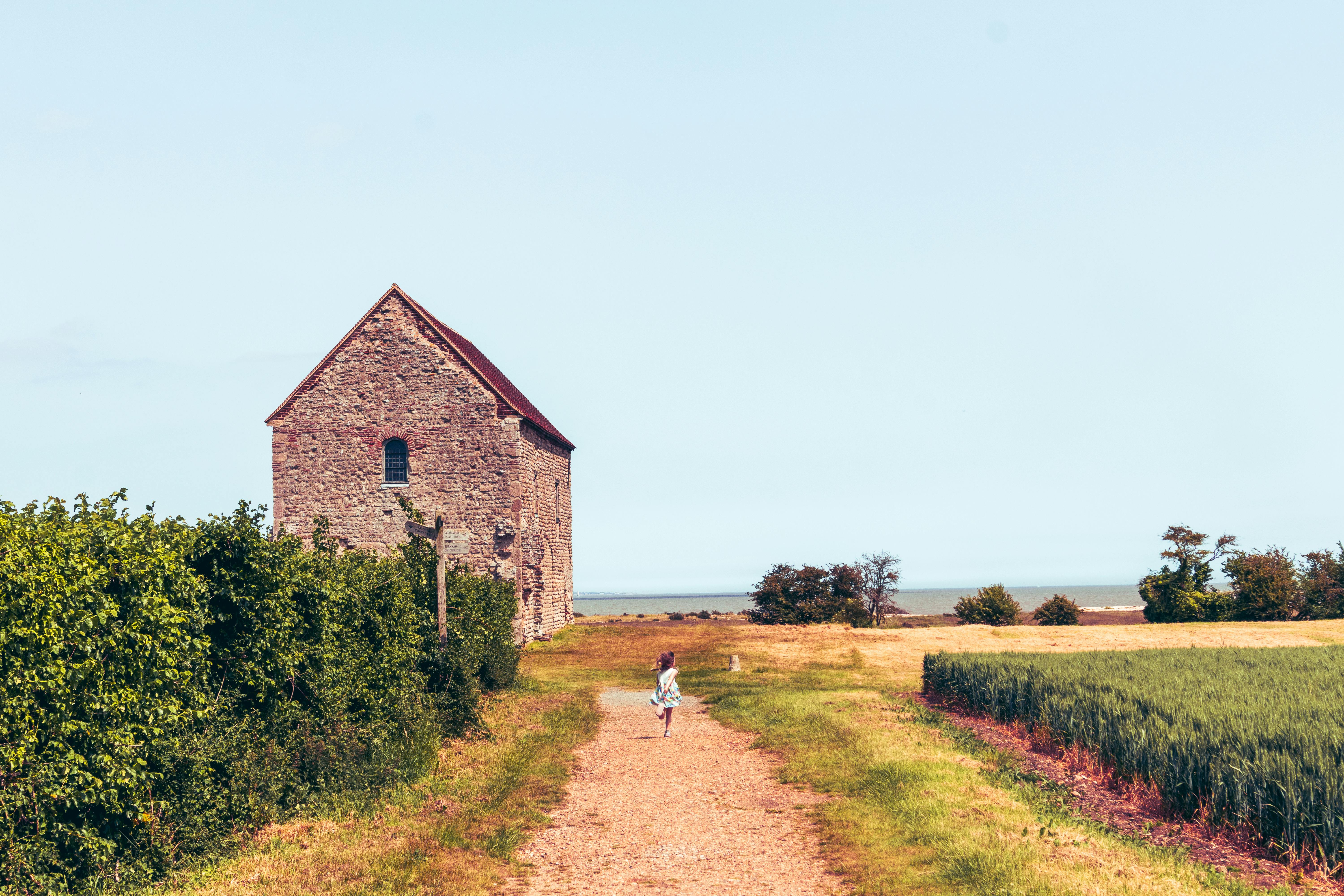 A serene medieval chapel by the sea with a girl walking on a rural path in Essex, England.