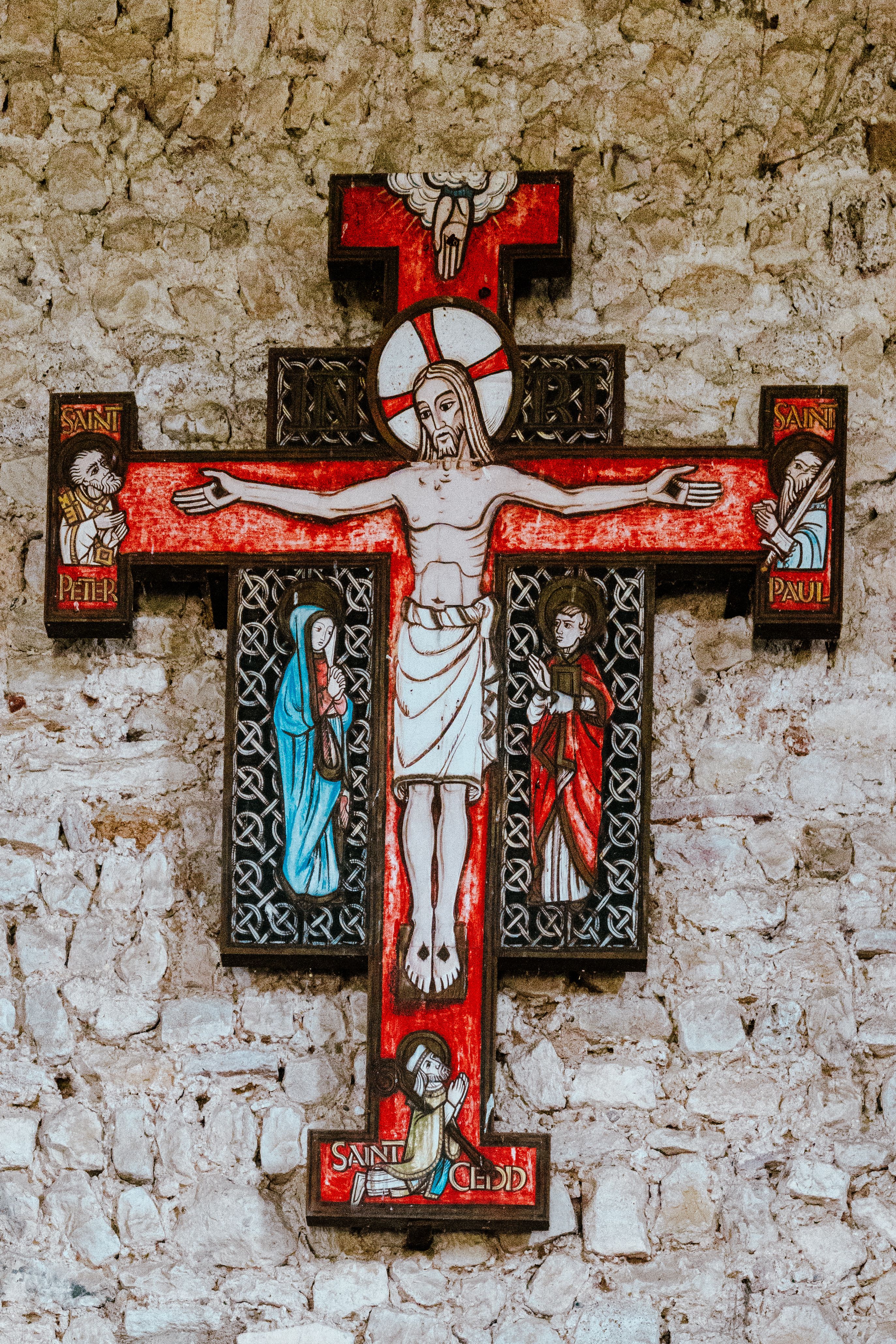 Medieval painted cross with Christ and saints on a stone wall in an ancient chapel.