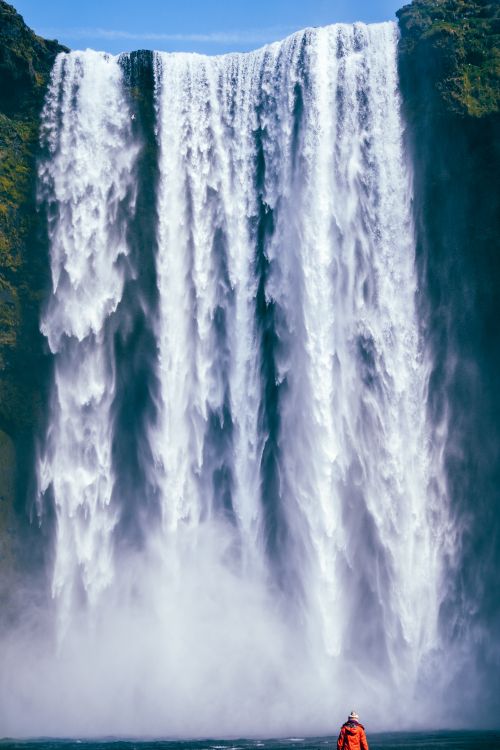 Free Dramatic view of Skogafoss waterfall with person in red coat in Iceland's adventure landscape. Stock Photo