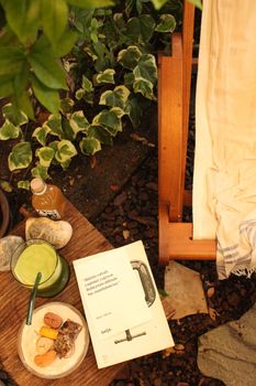 Warm outdoor scene with a book, snacks, drink, and chair amidst greenery.