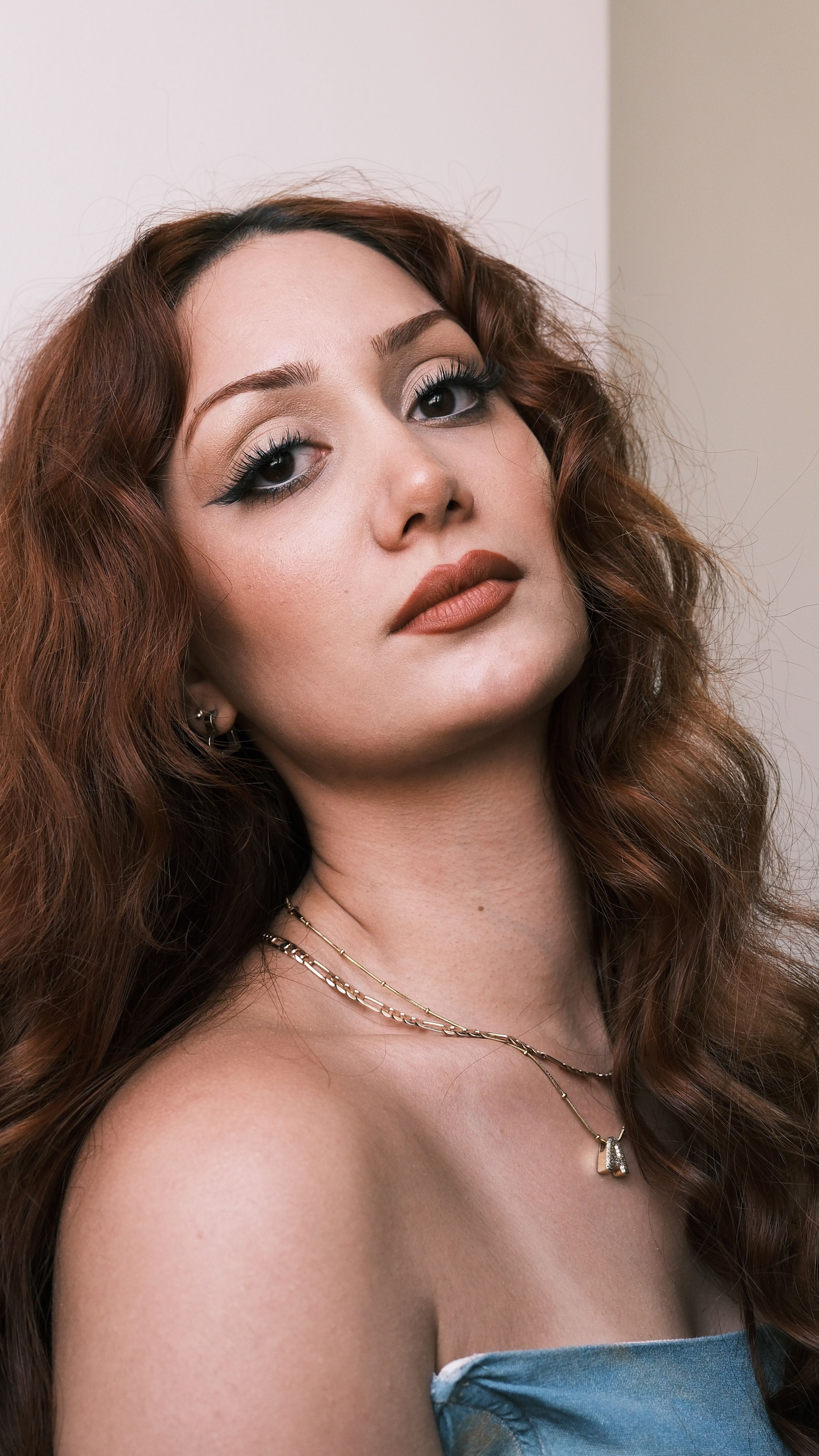 Elegant portrait of a woman with curly red hair, wearing makeup and jewelry.