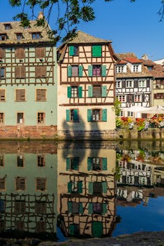 Picturesque Alsace timber-framed houses reflected in water on a sunny day.