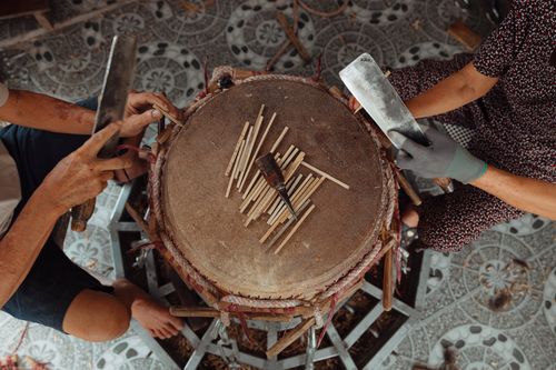 Free Aerial shot of two people crafting bamboo sticks with knives on a tiled floor. Stock Photo