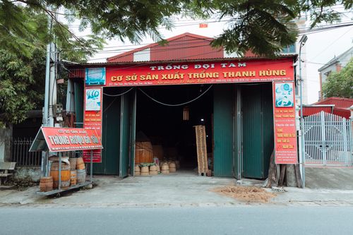 Free Front view of a traditional drum workshop in Duong Son, featuring wooden barrels and vibrant signage. Stock Photo