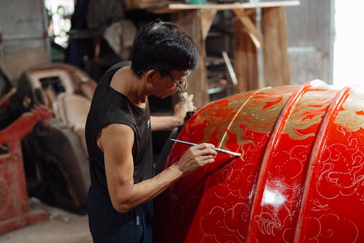 A skilled artisan paints a traditional gold and red design on a large drum, showcasing craftsmanship.