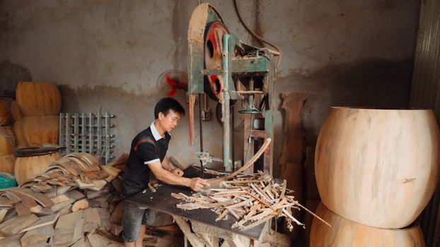Carpenter operating a woodworking machine in a workshop filled with wood pieces.