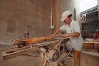 A carpenter in a dusty workshop precisely cuts wood using an industrial saw.