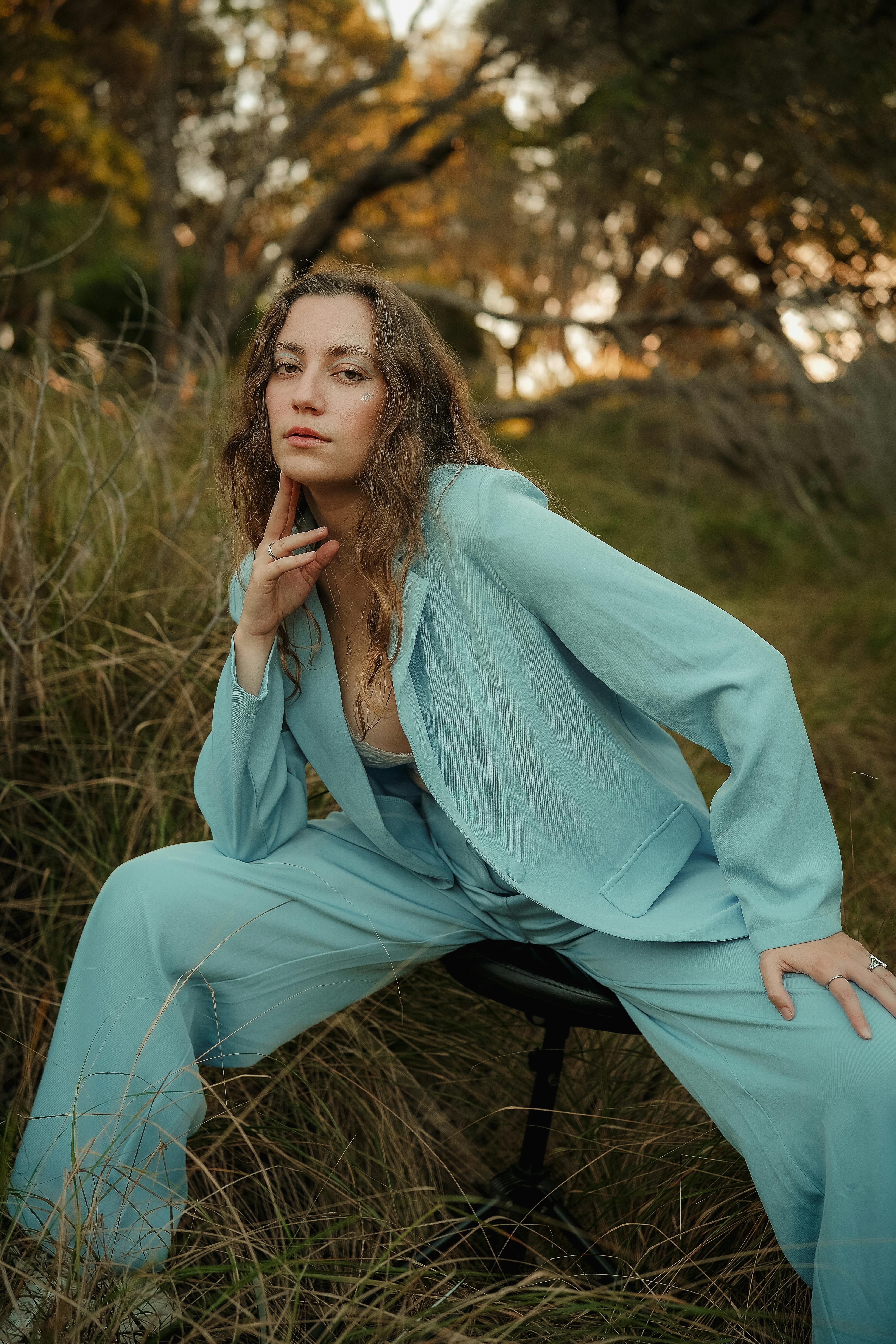 Fashionable woman in a light blue suit posing in a grassy outdoor setting with moody lighting.