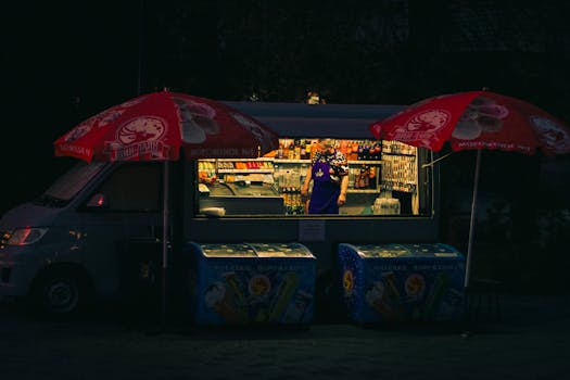 A food truck illuminated at night with colorful umbrellas and a vendor inside.