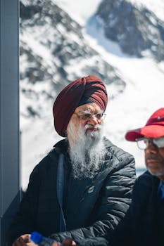 Elderly men wearing winter jackets and turbans, outdoors in snowy mountains.