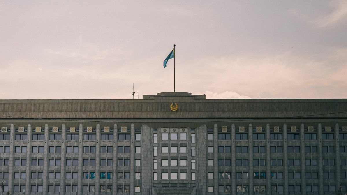 A grand government building with Kazakhstan flag in a clear sky.