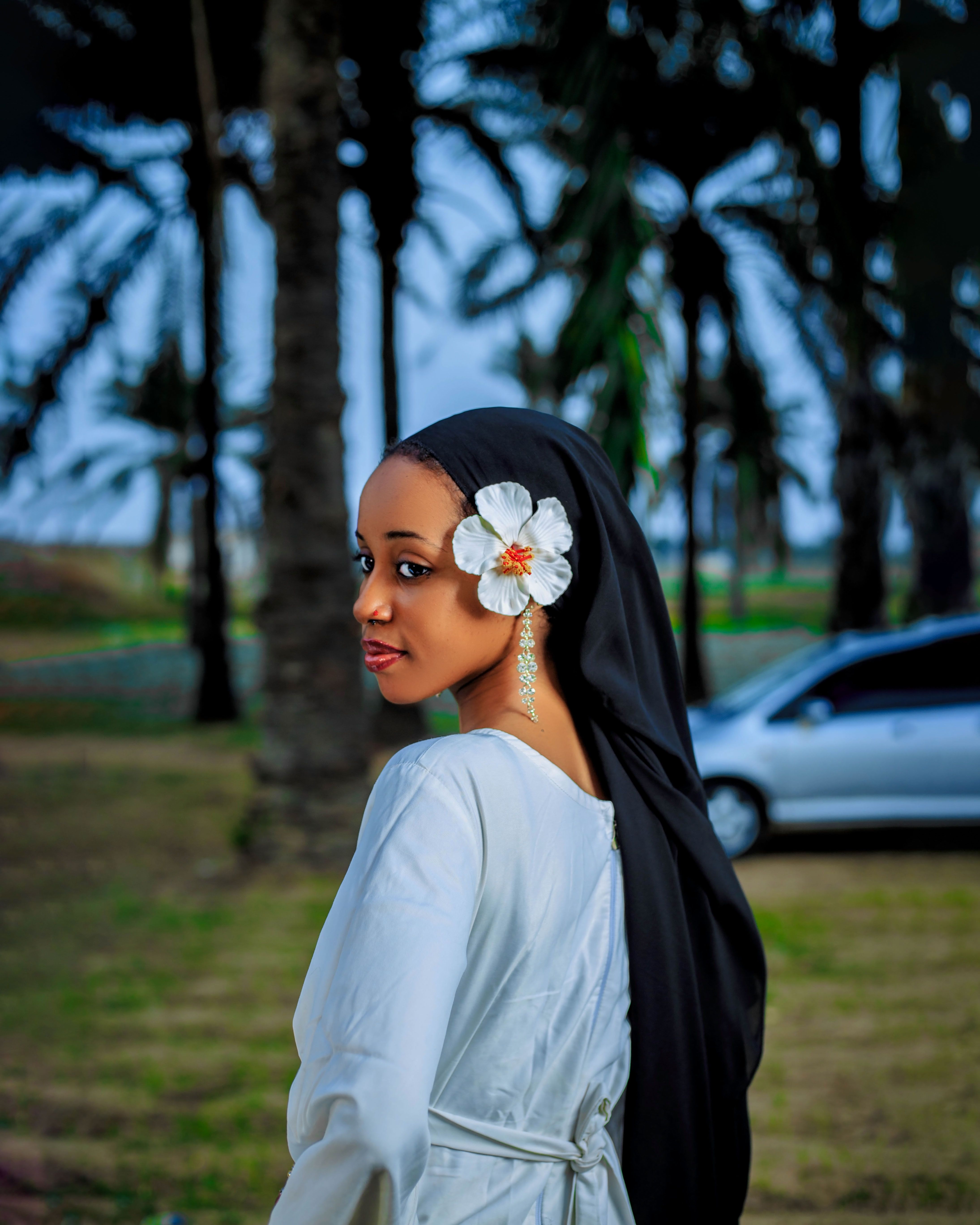 A woman wearing a white dress and floral headpiece in a lush, tropical park setting.