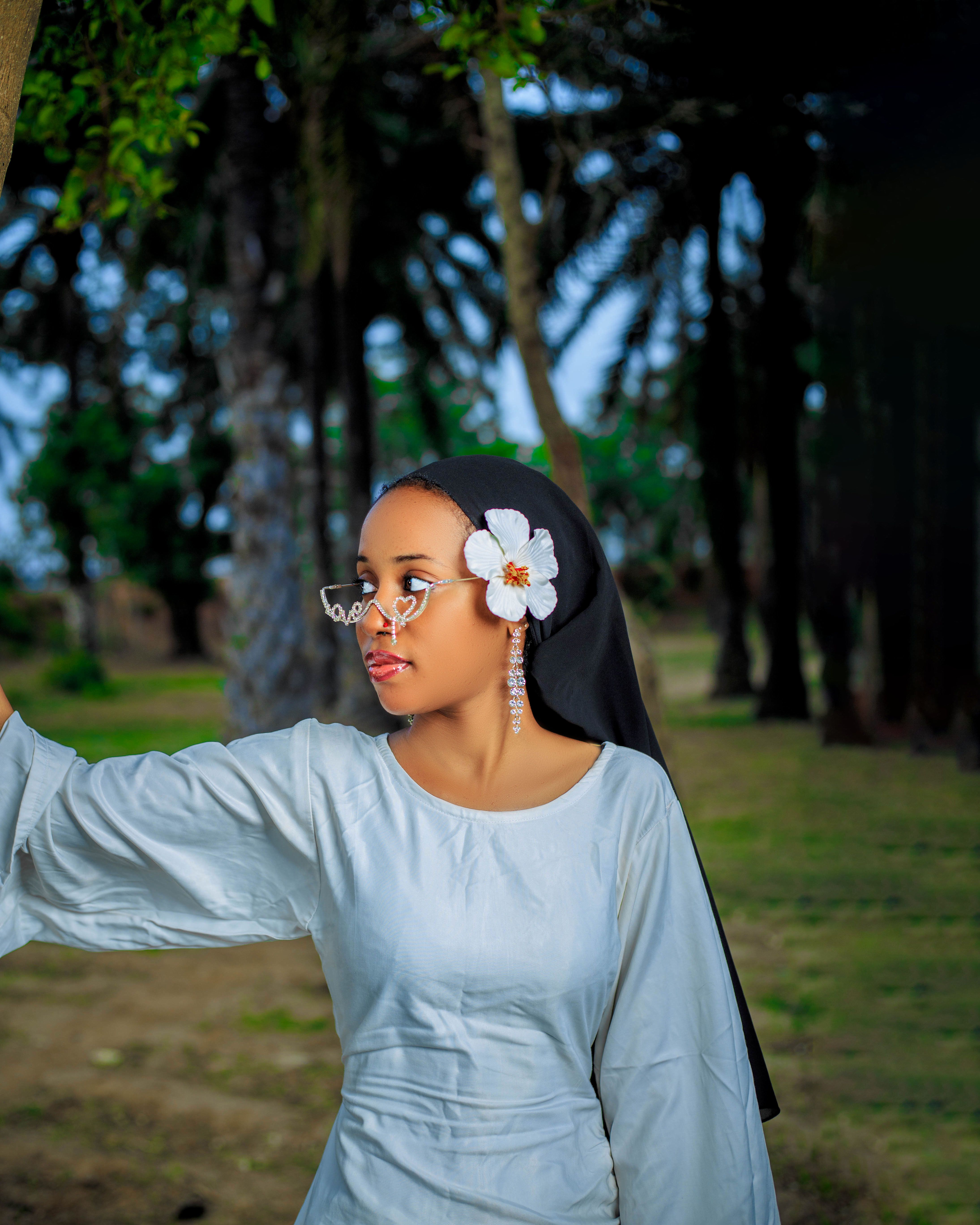 Young woman in hijab wearing glasses with flower accessory, set outdoors.