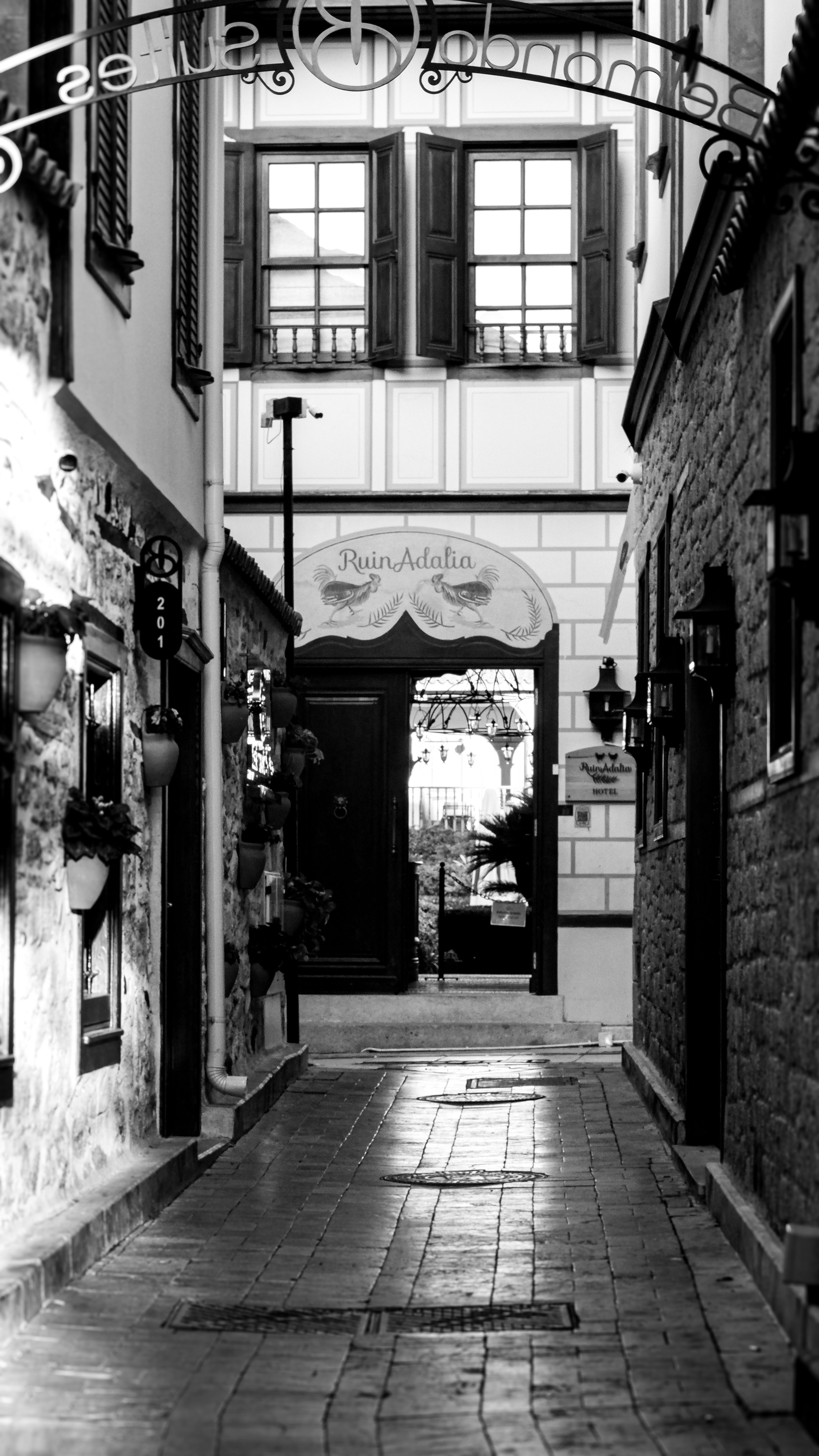 Black and white photo of a quaint narrow alleyway, showcasing charming stone buildings and vintage ironwork.