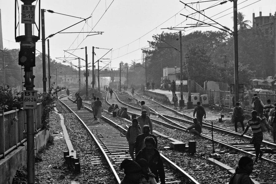 Crowded Indian railway tracks with people walking in a black and white setting.