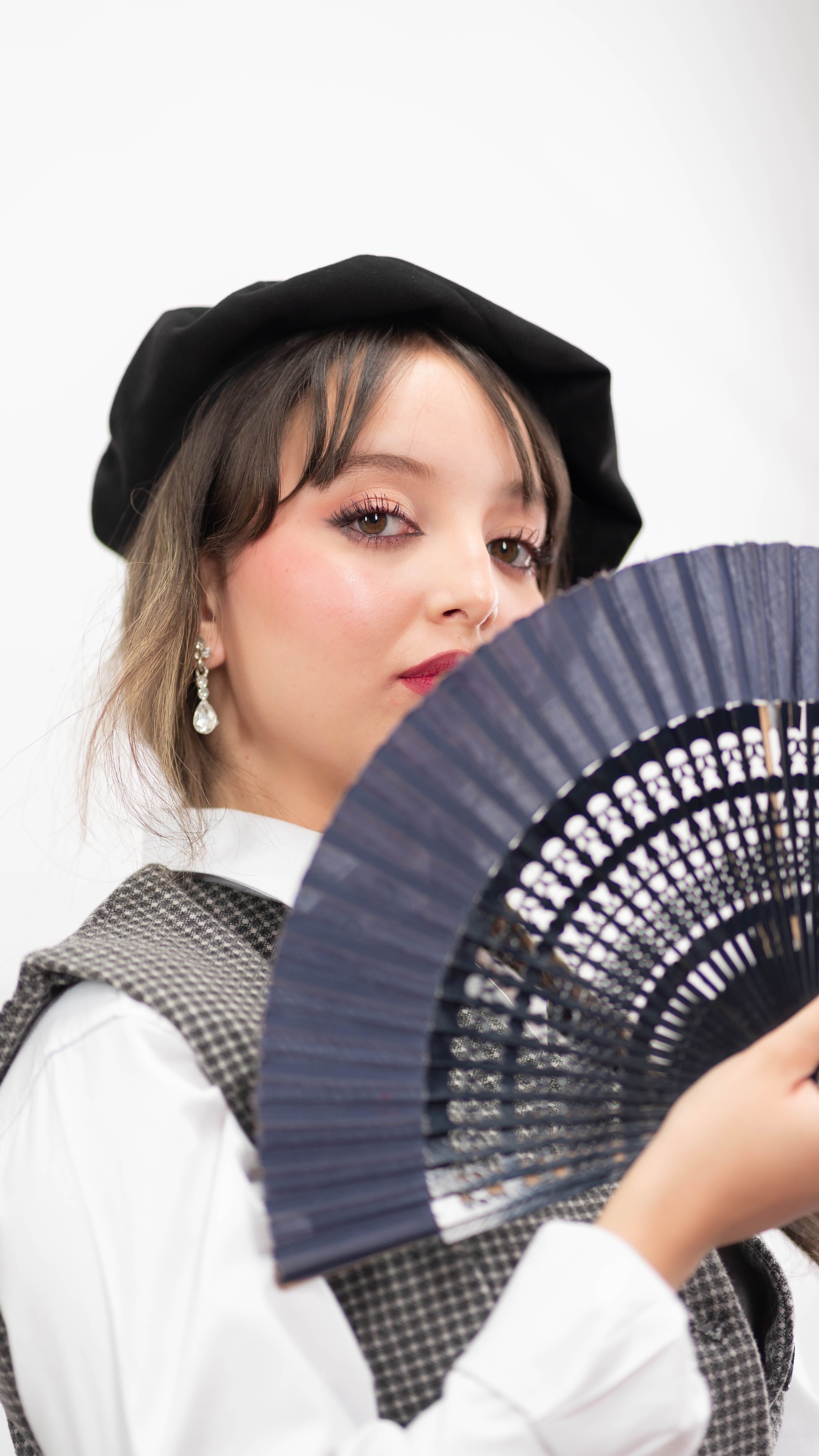 Stylish woman in a beret holding a lace fan, exuding elegance and sophistication.