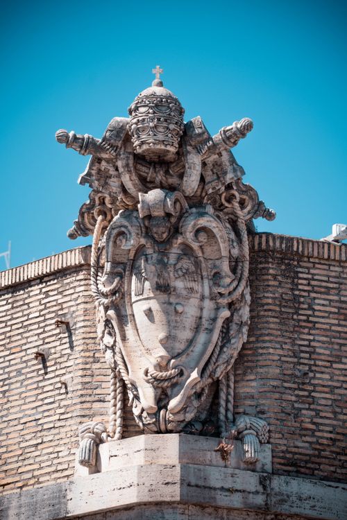 Free Close-up of an ornate papal coat of arms on a historical building in Vatican City against a clear blue sky. Stock Photo