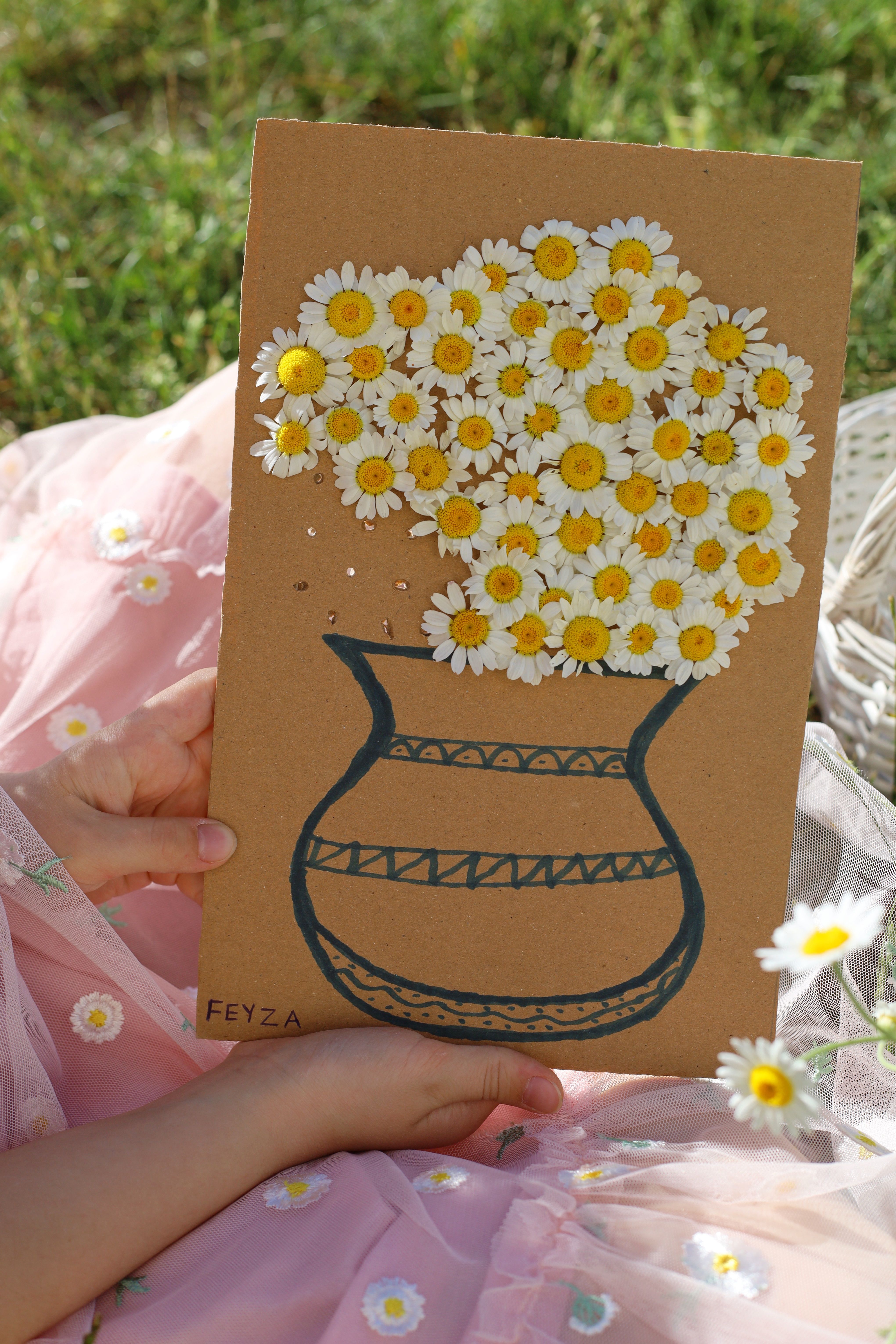 A delicate handmade floral arrangement featuring daisies on a cardboard vase.