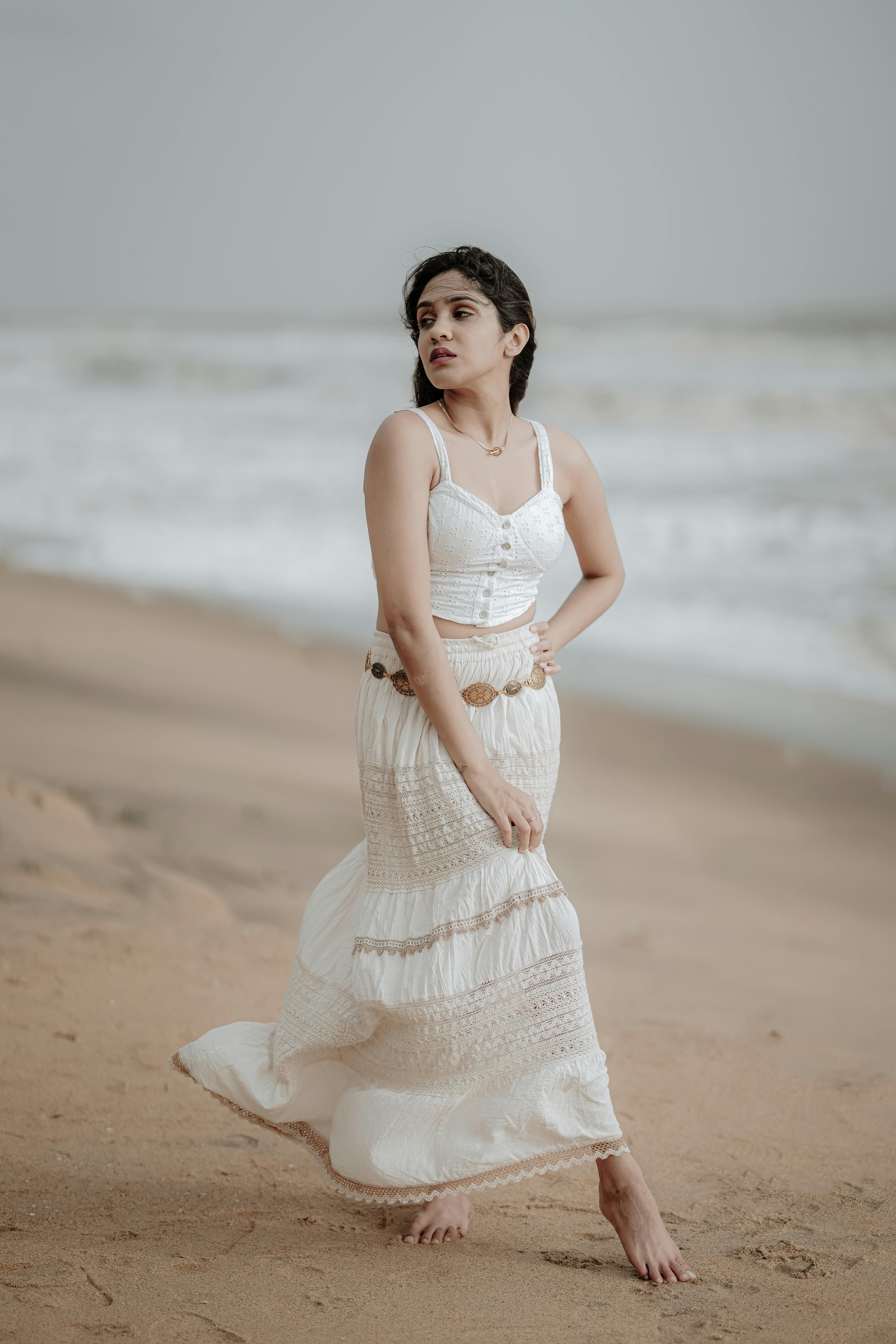 Woman in white dress enjoying a serene walk along the sandy beaches of Goa, India.