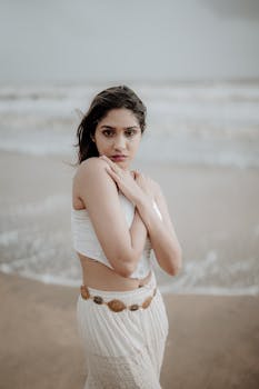Woman standing on a Kerala beach, embracing herself with a thoughtful gaze.
