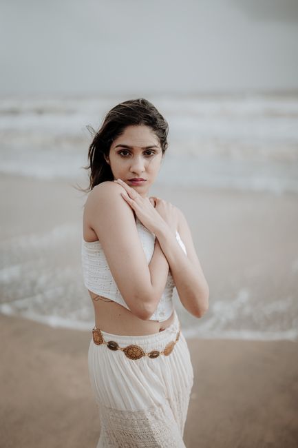 Woman standing on a Kerala beach, embracing herself with a thoughtful gaze.