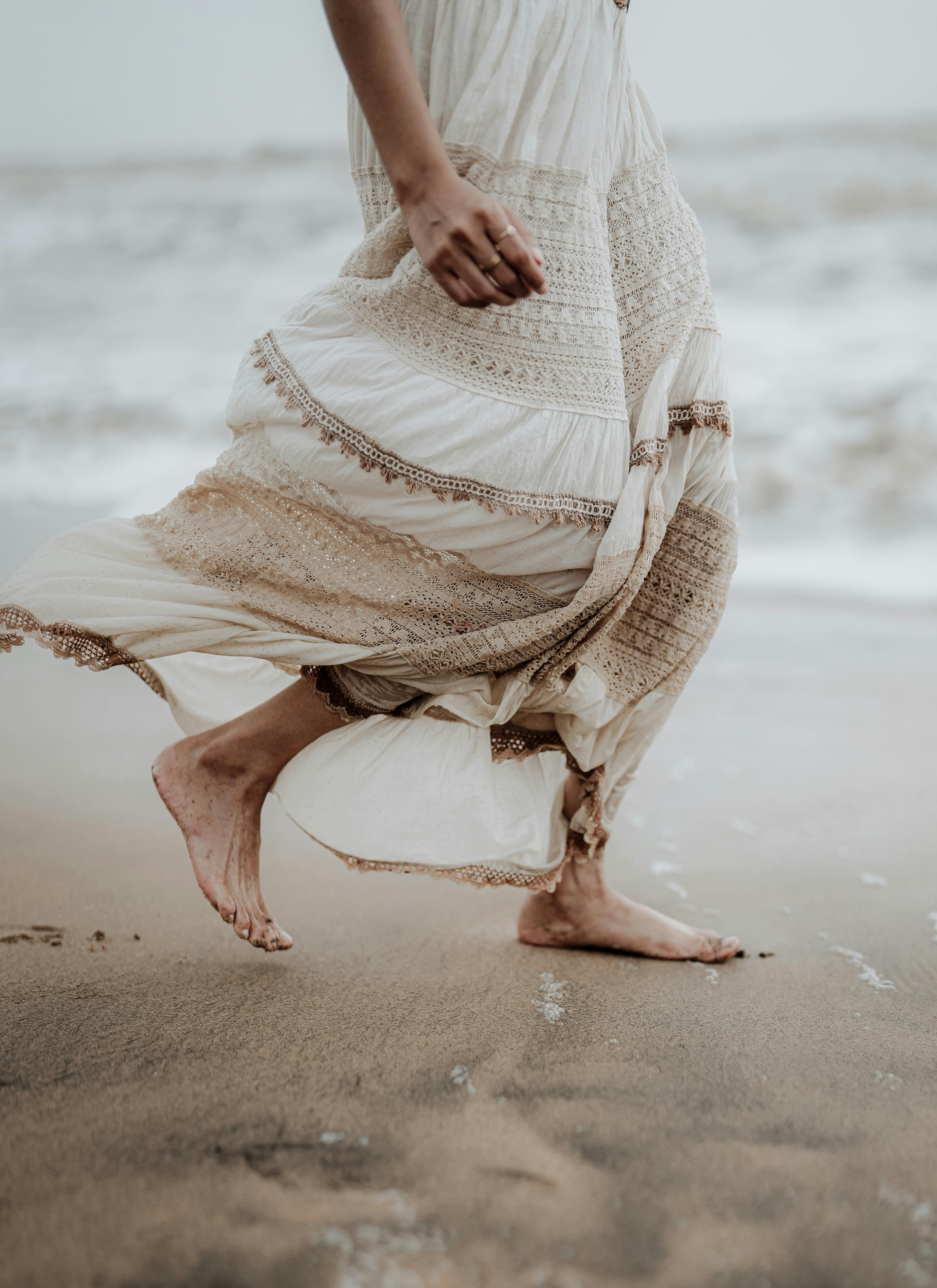穿着飘逸连衣裙的女人，赤脚走在沙滩上，享受着宁静的时刻