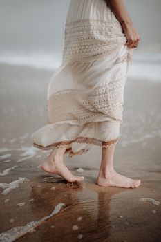 A serene scene of a woman in a white dress walking barefoot on a sandy beach in Kerala, India, capturing the essence of tranquility.