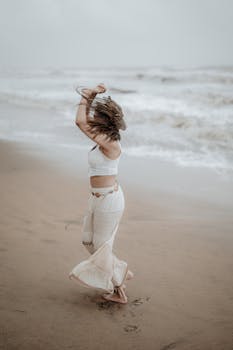 Joyful woman twirls on Irinjalakuda's beach, Kerala, India in a flowing dress.