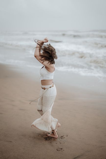 Joyful woman twirls on Irinjalakuda's beach, Kerala, India in a flowing dress.